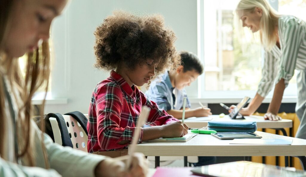 Diverse classmates doing task at lesson studying in classroom with teacher.