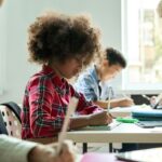 Diverse classmates doing task at lesson studying in classroom with teacher.