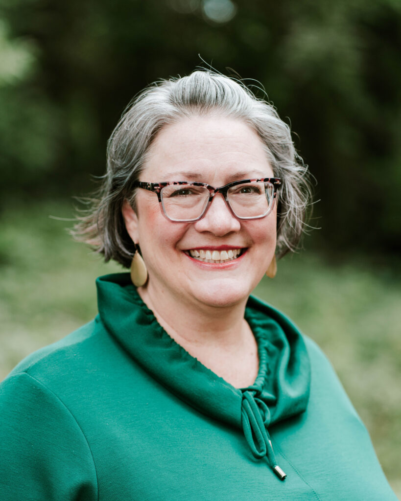 Smiling woman with gray hair and glasses in a green top, portrait.