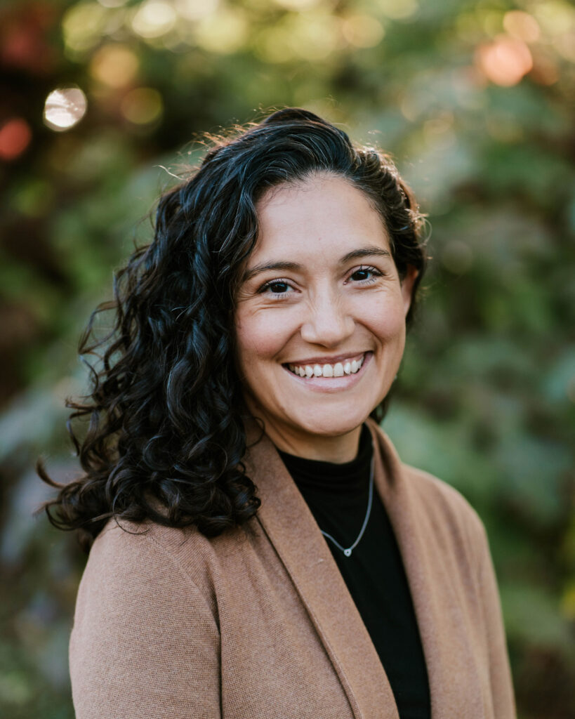 Portrait of a smiling woman with curly hair wearing a brown cardigan.