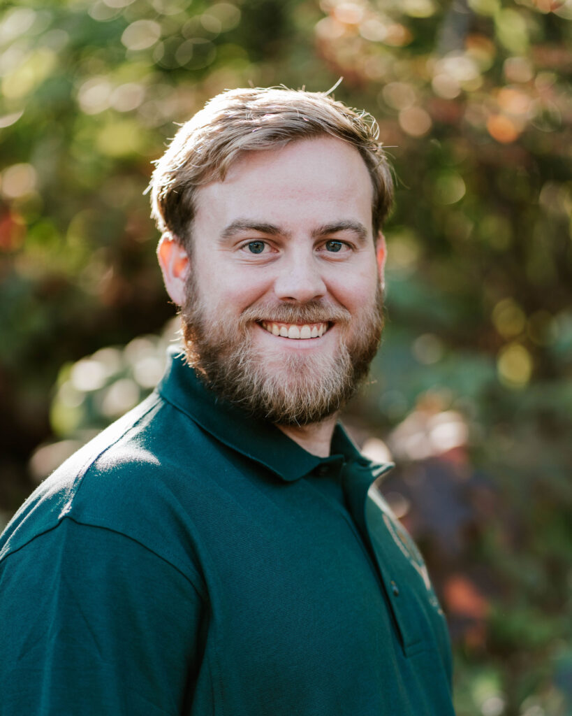 Portrait of a smiling man with a beard wearing a green polo shirt outdoors.