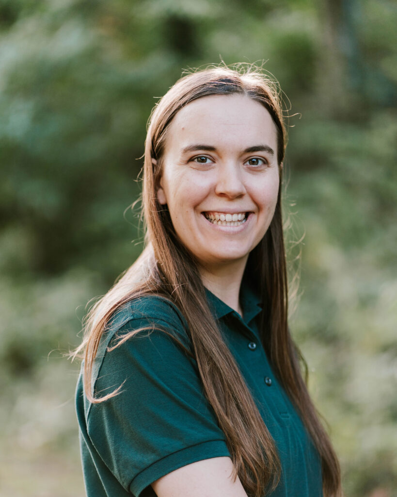 Portrait of a smiling graduate with long brown hair, wearing a green polo shirt outdoors.