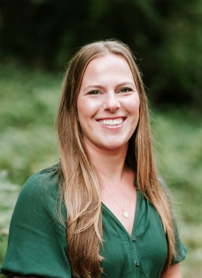 Portrait of a graduate in a green dress smiling outdoors.