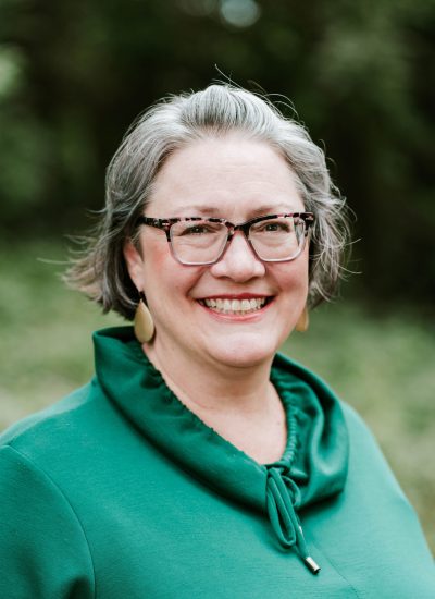 Smiling woman with gray hair and glasses in a green top, portrait.
