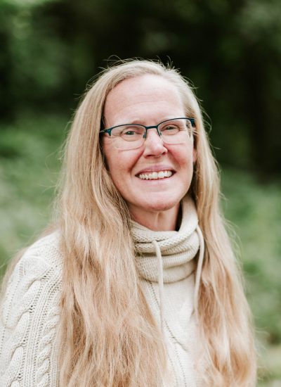 Portrait of a smiling woman with long blonde hair and glasses wearing a cream-colored sweater.