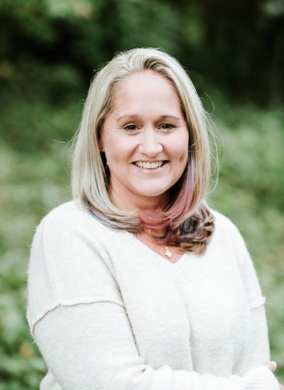 Smiling woman with blonde hair and colorful highlights wearing a white sweater.