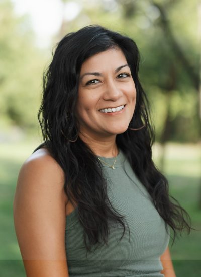 Smiling woman with dark hair and dimples in a green tank top outdoors